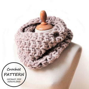 May include: A chunky, mauve-colored crochet cowl scarf made from thick yarn, featuring a small brown rectangular brand tag on the side. A circular graphic in the corner displays the text: Crochet PATTERN INSTANT PDF DOWNLOAD.