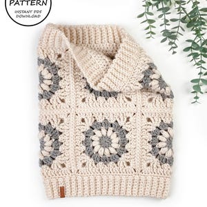 Puede incluir: Un cuello de punto de ganchillo con un patrón de cuadrados de la abuela en beige y gris. El cuello está doblado por la mitad y la textura de ganchillo es visible.