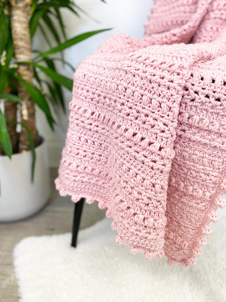 Pode incluir: Uma manta de croch&ecirc; rosa claro drapeada sobre uma cadeira. A manta apresenta um padr&atilde;o de ponto texturizado e uma borda ondulada. Esta manta macia e feita &agrave; m&atilde;o &eacute; um item de decora&ccedil;&atilde;o para casa.