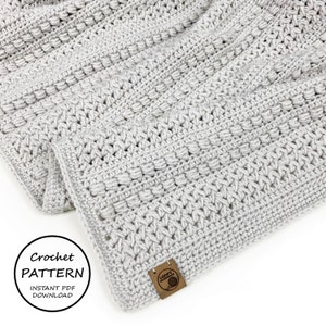 Peut inclure: Une couverture en crochet grise avec un motif de points texturés. La couverture est pliée en deux et porte une étiquette brune avec le texte "Loopy Handmade". Le texte "Crochet Pattern Instant PDF Download" est également visible sur l'image.