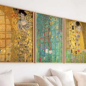 Peut inclure: Trois impressions d'art encadrées représentant des peintures célèbres de Gustav Klimt. La première impression est un portrait d'une femme dans une robe dorée à motif géométrique. La deuxième impression est un paysage avec un fond bleu et vert et des fleurs. La troisième impression est une représentation de deux figures s'embrassant dans une étreinte dorée.