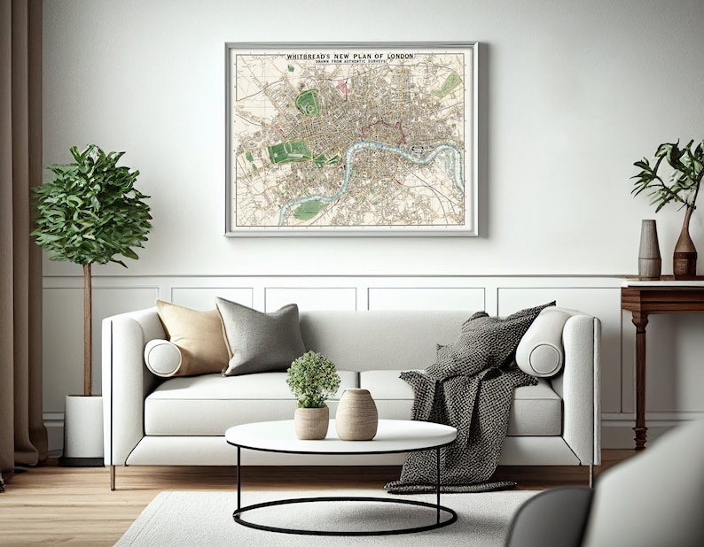 May include: A white sofa with beige and gray throw pillows and a black throw blanket. A vintage map of London titled "Whitebread's New Plan of London" hangs on the wall above the sofa. A round coffee table with a white top and black metal base sits in front of the sofa.