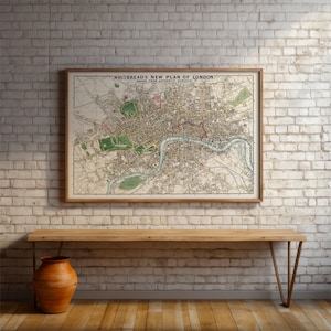 May include: A vintage map of London, titled "Whitbread's New Plan of London, Drawn from Authentic Surveys", framed in a light wood frame and hanging on a white brick wall.