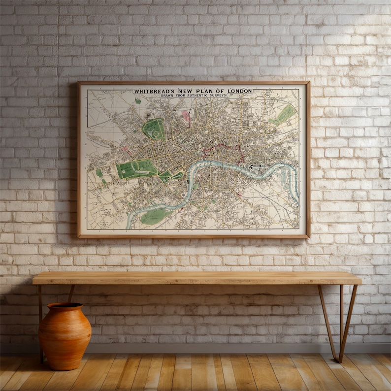 May include: A vintage map of London, titled "Whitbread's New Plan of London, Drawn from Authentic Surveys", framed in a light wood frame and hanging on a white brick wall.