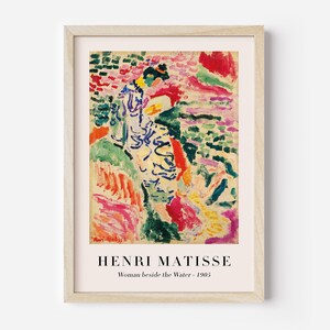 May include: A framed print of a painting by Henri Matisse titled "Woman beside the Water - 1905". The painting features a woman in a white and blue dress standing in a landscape of colorful brushstrokes.