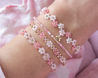 May include: Four pink and white beaded bracelets with gold accents. Each bracelet features a flower design.