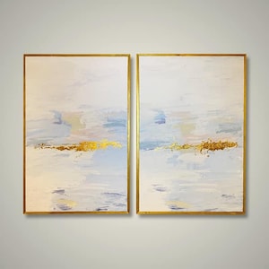 May include: Two abstract paintings in gold frames. The paintings are a light blue and white with gold accents. The paintings are side by side.