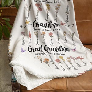 May include: White fleece blanket with a floral design and names of family members. The text reads "Mom Growing since 1977", "Grandma Growing since 1999", and "Great Grandma Growing since 2022".
