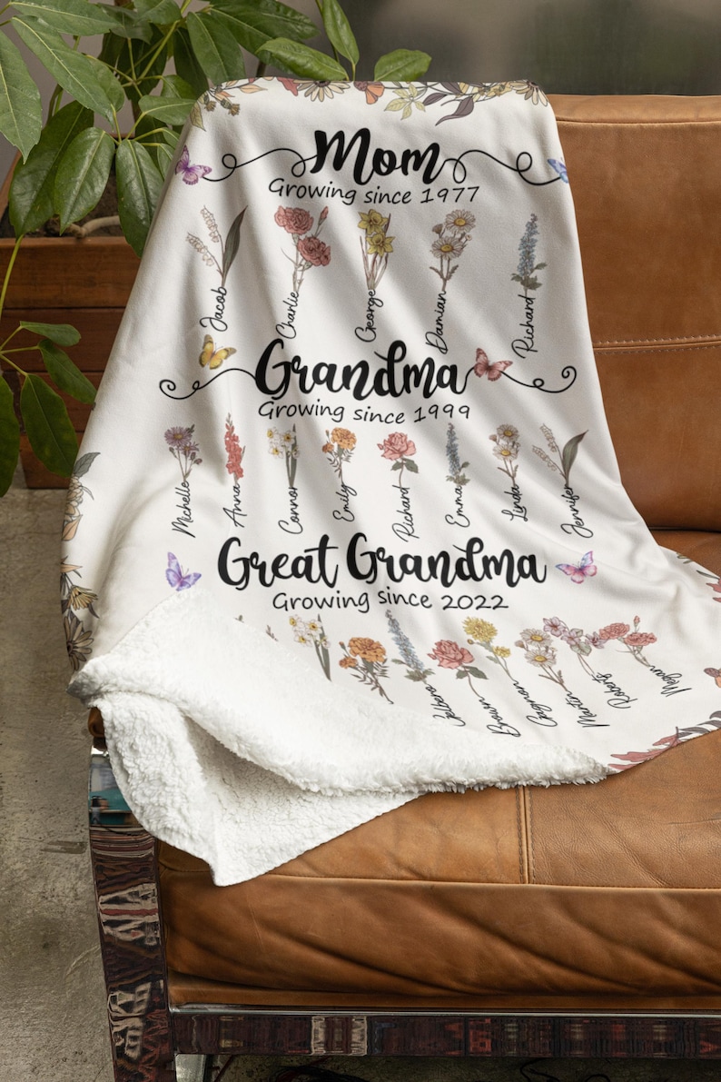 May include: White fleece blanket with a floral design and names of family members. The text reads "Mom Growing since 1977", "Grandma Growing since 1999", and "Great Grandma Growing since 2022".