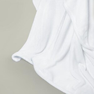 May include: A white plush blanket with soft, fluffy texture. The blanket is folded and draped over a surface, showcasing its smooth and luxurious feel.