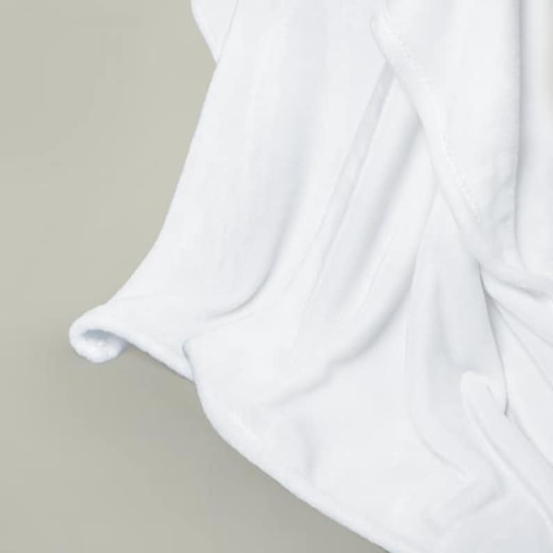 May include: A white plush blanket with soft, fluffy texture. The blanket is folded and draped over a surface, showcasing its smooth and luxurious feel.