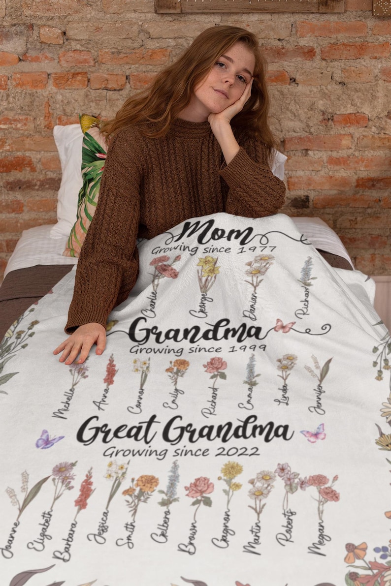 May include: White floral blanket with the text "Mom Growing since 1977", "Grandma Growing since 1999", and "Great Grandma Growing since 2022". The blanket features a floral design with names written on each flower.