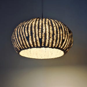 May include: A textured, spherical pendant light fixture. The light has a dark, ridged exterior and a bright, white interior. The light hangs from a single cord and casts a warm glow.