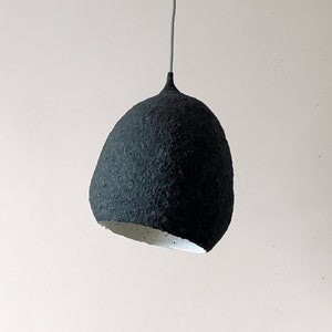 May include: A black paper pendant light with a textured surface. The light is hanging from a white ceiling.