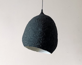 Suspension black papier maché lamp. The irregular oval of the lampshade resembles a drop or lump of concrete.  White inside. Model 18B.