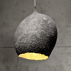 May include: A black, textured, round pendant light with a gold interior. The light is hanging from a ceiling.