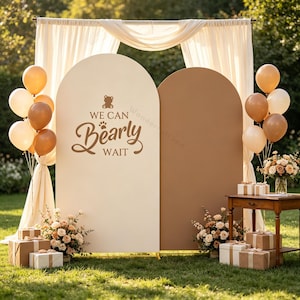 Pode incluir: Dois painéis de fundo arqueados em creme e castanho claro, com um ícone de urso castanho e o texto WE CAN Bearly WAIT. A decoração inclui cortinas de tecido creme, cachos de balões castanhos e creme, arranjos florais e caixas de presente.
