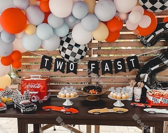 May include: A birthday party decoration set with a black and white checkered balloon, black balloons that spell out "TWO FAST", and a black and white checkered banner. The balloons are strung together in a garland and are surrounded by other balloons in shades of blue, orange, and white.