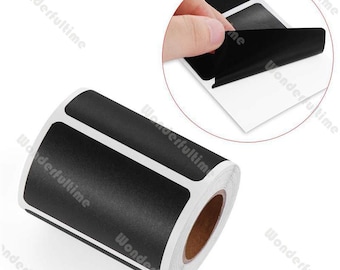 May include: A roll of black rectangular labels with white borders. A hand is peeling a label from a sheet of similar labels in the upper right corner. The labels are on a white background.