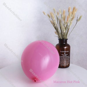 May include: A single, large, hot pink balloon. The balloon is deflated and has a small opening at the bottom. The balloon is sitting on a white surface.