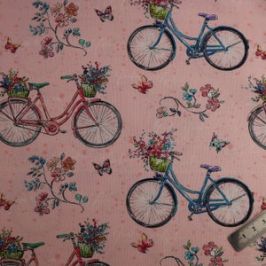 May include: A pink fabric design with a repeating pattern of bicycles, butterflies, and flowers. The bicycles are in red and blue, with flower baskets. Butterflies and floral vines are scattered across the fabric. The design has a vintage feel.