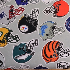 May include: A light grey fabric with a repeating pattern of American football helmets. The helmets are in various colours, including orange, black, green, and blue, with white outlines. The helmets represent different teams.