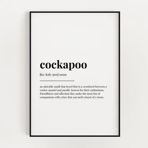 May include: A framed print with the word "cockapoo" in a bold, black font. Below the word is the pronunciation and a definition describing the dog breed as a cross between a cocker spaniel and poodle.