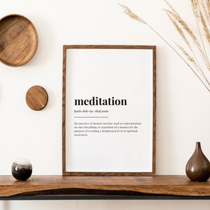 Peut inclure: Une impression encadr&eacute;e noire avec le mot "m&eacute;ditation" et sa d&eacute;finition dans une police blanche simple. L'impression est accroch&eacute;e &agrave; un mur blanc avec une d&eacute;coration en bois et un vase d'herbe s&egrave;che.