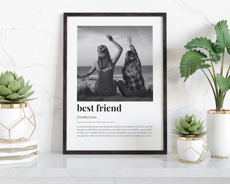 May include: Black and white photo of two friends with their arms raised in the air, printed on a white background with the text "best friend" and a definition below. The photo is framed in a black frame.