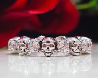 May include: A silver ring with a row of small skulls and clear cubic zirconia stones.