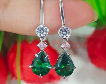Puede incluir: Pendientes de plata con una piedra preciosa verde en forma de lágrima, una piedra preciosa rosa cuadrada más pequeña y una piedra preciosa redonda transparente.