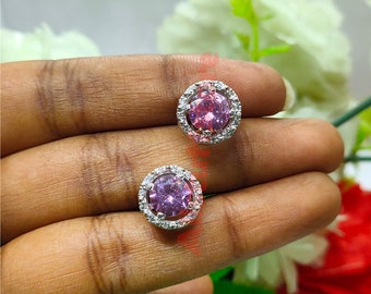 May include: A pair of silver stud earrings with a pink gemstone surrounded by a halo of smaller clear gemstones.