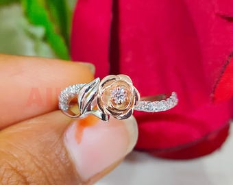 以下が含まれることがあります： 中央にダイヤモンドが1つ付いた、ローズゴールドの花のデザインのシルバーリング。花には横に葉が付いています。