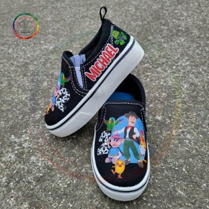 Peut inclure: Chaussures &agrave; enfiler noires avec des personnages de dessins anim&eacute;s color&eacute;s et le nom "MICHAEL" en rouge. Les chaussures ont des semelles blanches et une tige noire, avec une tirette au talon. Le design comprend divers personnages et le chiffre 2.