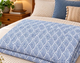 May include: A folded quilt featuring a repeating blue and white fan-shaped pattern. The fabric displays a series of concentric semicircles in deep blue ink against a light cream background, creating a structured, geometric design across the textile.