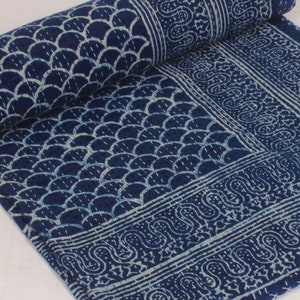 May include: Indigo blue and white patterned quilt. The quilt features a repeating scallop design and a decorative border with a paisley-like pattern. The quilt is partially rolled up, showcasing the detailed design.