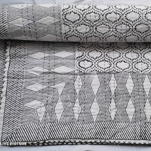 May include: A white cotton quilt with a black geometric pattern. The quilt is folded in half and shows a variety of different patterns, including diamonds, circles, and squares.