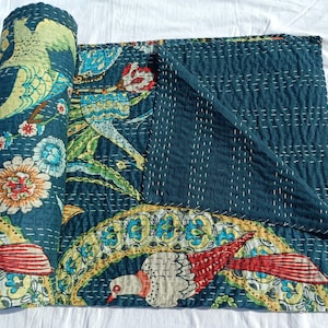 May include: A rolled-up teal quilt with a vibrant bird and floral design. The quilt features a repeating pattern of colorful birds, flowers, and foliage in shades of red, yellow, and blue. The quilt is hand-stitched with white thread, creating a textured appearance.