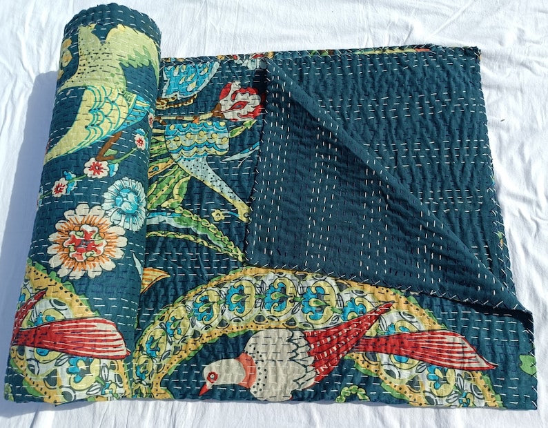 May include: A rolled-up teal quilt with a vibrant bird and floral design. The quilt features a repeating pattern of colorful birds, flowers, and foliage in shades of red, yellow, and blue. The quilt is hand-stitched with white thread, creating a textured appearance.