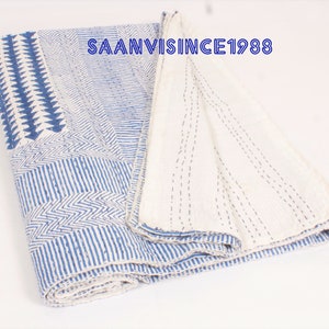 May include: A folded cotton quilt featuring a blue and white geometric pattern with visible running stitch details. The fabric displays various linear, chevron, and triangular motifs. The text SAANVISINCE1988 is printed in blue on the quilt surface.