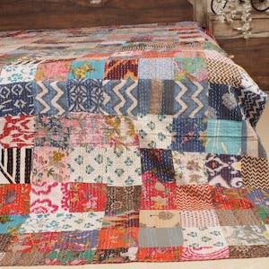 Könnte beinhalten: Eine farbenfrohe Patchwork-Decke aus verschiedenen Stoffen in Blautönen, Rot, Rosa und Braun. Die Decke besteht aus Quadraten unterschiedlicher Größe und Muster, die ein einzigartiges und auffälliges Design ergeben.