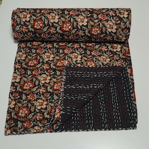 May include: A folded cotton quilt featuring a dark background with a repeating floral pattern in shades of red, cream, and brown. The reverse side displays a solid black fabric with visible white and red running stitch embroidery throughout.