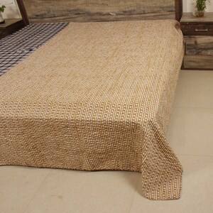 May include: A brown and white patterned kantha quilt with a subtle geometric design. The quilt is folded and displayed on a bed.