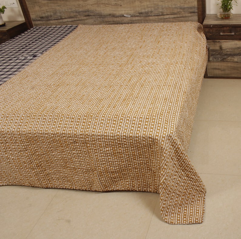 May include: A brown and white patterned kantha quilt with a subtle geometric design. The quilt is folded and displayed on a bed.