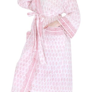 May include: A white and pink patterned robe with a matching belt. The robe features a leaf design and decorative trim on the sleeves, pockets, and edges. The robe is knee-length.