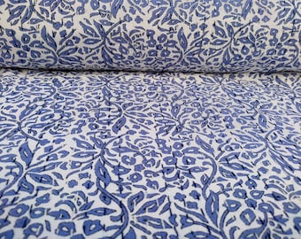 Puede incluir: Un rollo de tela con un patrón floral azul repetido sobre un fondo blanco. El diseño presenta hojas estilizadas y pequeñas formas florales. La tela está enrollada, mostrando la continuidad del patrón.