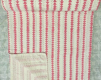 May include: A rolled-up white quilt with a repeating pattern of pink triangles. The triangles are arranged in vertical rows, creating a striped effect. The quilt is folded over, revealing a corner of the same pattern.