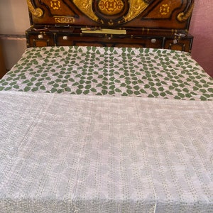 May include: A reversible bedspread featuring a white side with subtle, light green stitched patterns and a contrasting side with a repeating green leaf motif on a white background. The fabric displays visible running stitch details throughout.