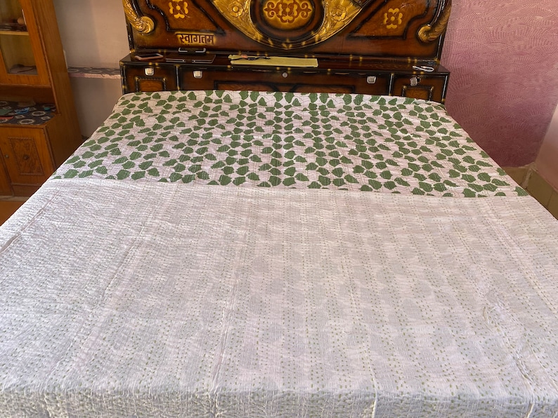 May include: A reversible bedspread featuring a white side with subtle, light green stitched patterns and a contrasting side with a repeating green leaf motif on a white background. The fabric displays visible running stitch details throughout.