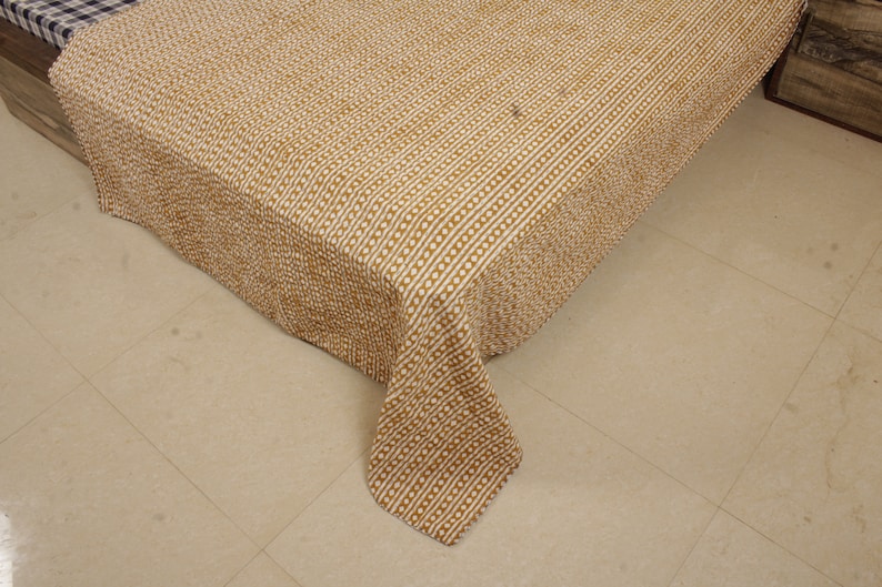 May include: A brown and white patterned quilt with a textured surface. The quilt is folded and draped over a bed.